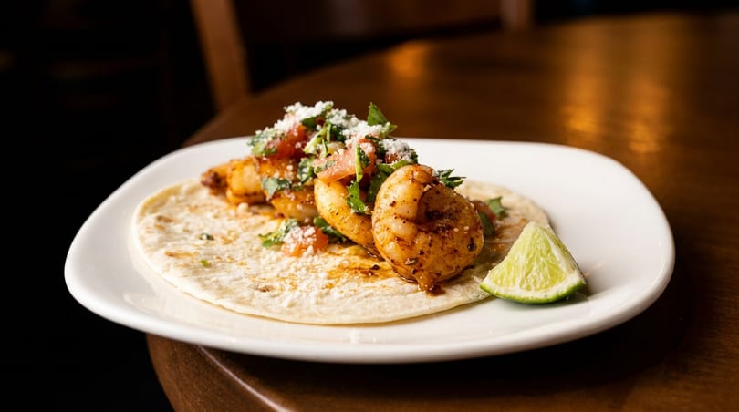 Shrimp taco with pico de gallo, cheese, and cilantro, served with a lime wedge.