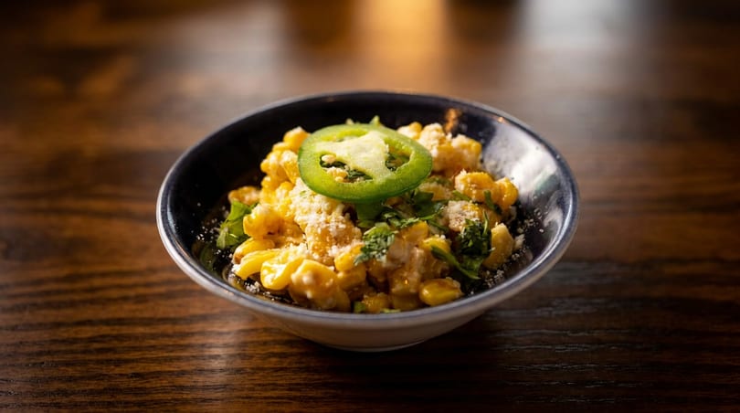A bowl of macaroni and cheese topped with a jalapeño slice, cilantro, and grated cheese.